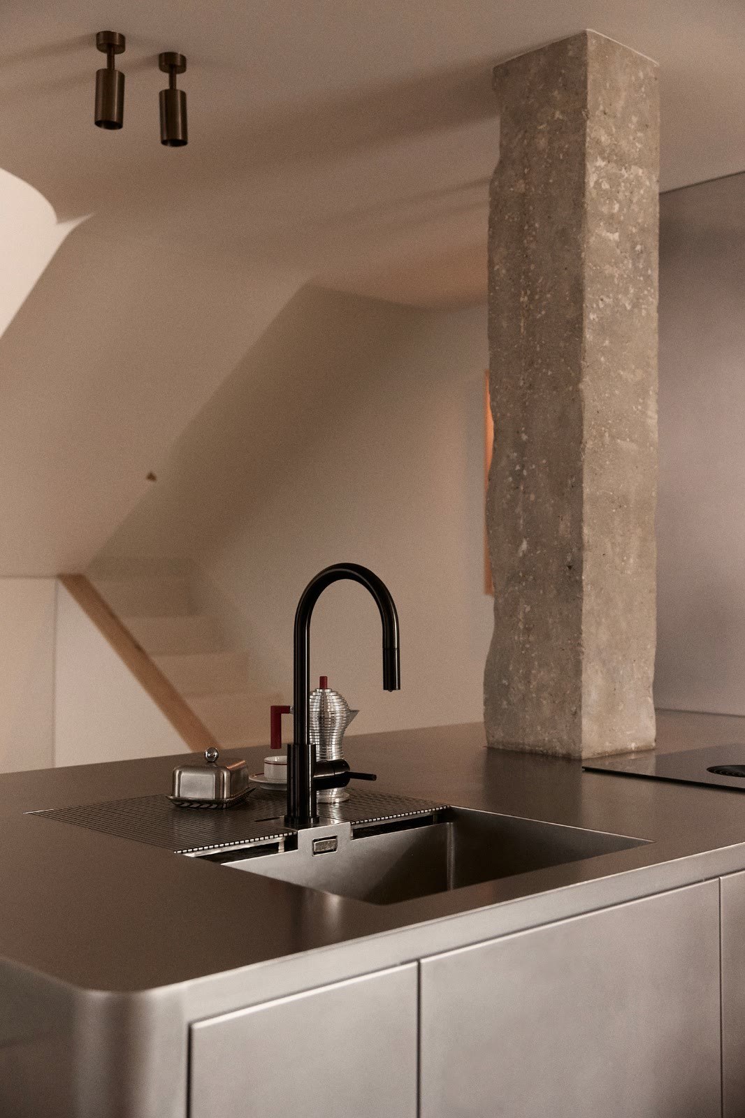 Cuisine sur mesure en inox et colonne de pierre sous une toiture mansardée